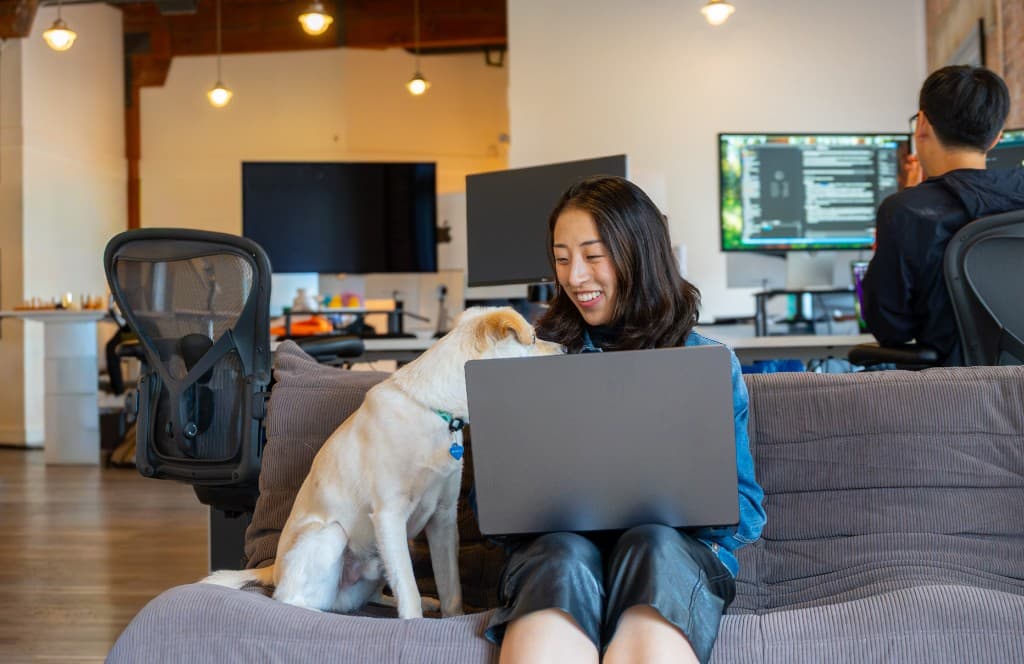 A Cohorvaer working from the office couch beside a dog